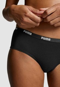 Schwarze Baumwollunterhose mit glatter Textur, ausgestattet mit einem breiten elastischen Bund, der mit dem weißen "PUMA"-Logo verziert ist.