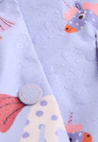 Gros plan de gouttes d'eau sur un tissu violet avec des imprimés d'animaux colorés et un bouton rond.