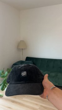 Μαύρο καπέλο από κορδούρα με καμπύλη γείσο, με τετράγωνο εμβληματικό κεντημένο σχέδιο που γράφει "Santa Cruz". Κρατείται στο χέρι πάνω σε ουδέτερο φόντο.