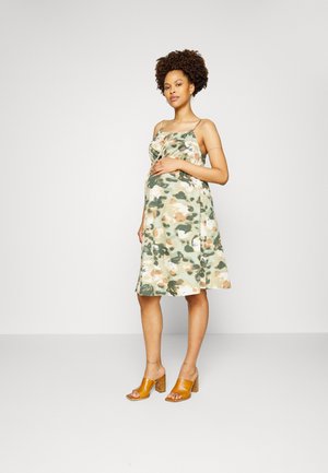 Vestido com padrão de camuflagem em tons de verde, bege e castanho, com um corte solto e alças finas. Usado com sandálias de salto bloco amarelas.