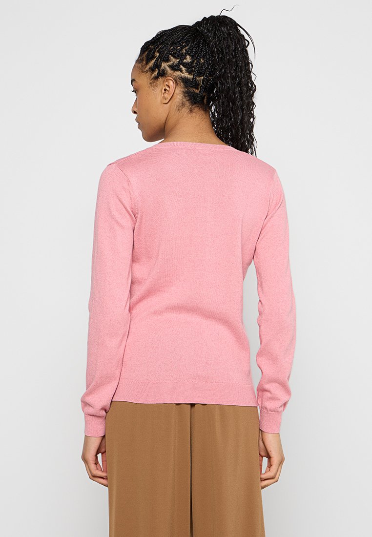 Maglione rosa lavorato a maglia con maniche lunghe e scollo rotondo, caratterizzato da un design aderente, una consistenza liscia e polsini a coste. Indossato con pantaloni marroni.