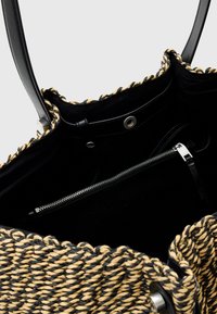 Borsa a tracolla intrecciata nera e beige con un'esterno testurizzato, un interno liscio, manici in pelle e una tasca con zip all'interno.