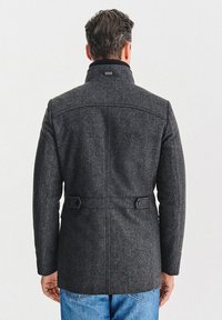 Szary wełniany płaszcz z wysokim kołnierzem, z tylnym rozcięciem i dwoma regulowanymi paskami. Tekstura jest gładka, a krój dopasowany i strukturalny.