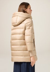 Beżowa puchowa kurtka z kapturem, z poziomymi pikowanymi sekcjami, bocznymi kieszeniami i ściągaczami przy rękawach. Tkanina ma gładką, lekko błyszczącą fakturę.