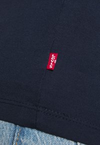 Gros plan sur un tissu bleu marine avec une couture visible et une petite étiquette rouge Levi's près d'un jean en denim bleu clair.