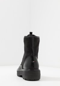 Schwarze Knöchel-Stiefel mit einem Obermaterial aus Canvas und glänzenden Lederakzenten, einer robusten Gummisohle und einer Zuglasche hinten für ein einfaches Anziehen.
