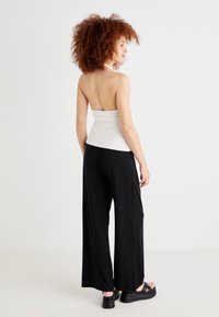 White strapless top with a fitted design paired with loose black wide-leg pants. Model wears black platform sandals. Textured, smooth materials.