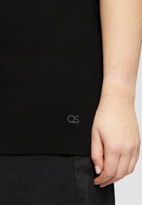 Zwarte korte mouwen t-shirt van katoen, met een klein geborduurd "QS" logo bij de zoom. De stof is glad en aansluitend.