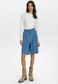 Kék csíkos farmer rövidnadrág magas derékkal és gombos záródással, hosszú ujjú fehér felsővel és bézs bokacsizmával párosítva.