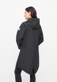 Chaqueta negra impermeable con capucha, cintura ajustada y dobladillo a la altura del muslo. Presenta una textura sutil y un parche con logo en el hombro.