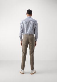 Camicia a righe blu e bianca con bottoni abbinata a pantaloni slim-fit beige chiaro e sneakers bianche con suola in gomma, vista da dietro.