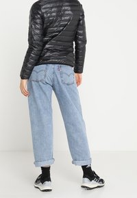 Sort dunjakke, blå denim jeans med opfoldede cuffs og sorte sportssko. Glat stof, løs pasform og klassisk fem-lommeredesign.