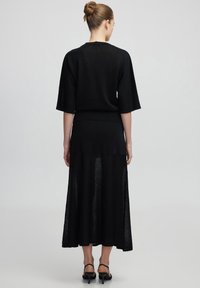 Robe en tricot noire avec des manches courtes et larges, de longueur midi. Présente un corsage ajusté, une jupe évasée et une couche transparente subtile au bas.