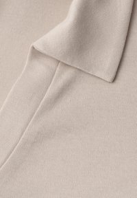 Tissu tricoté beige avec un col plié et une couture visible, montrant une texture douce et un motif côtelé fin.