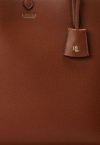 Brun strukturert skinnveske med gullfargede "Lauren Ralph Lauren" og "RL" logoer og en festet skinnetikett.