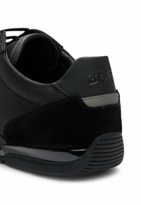 Czarne trampki z teksturowaną cholewką wykonana z materiałów siatkowych i zamszowych, o smukłym designie, gumowej podeszwie oraz wytłoczonym logo na pięcie.
