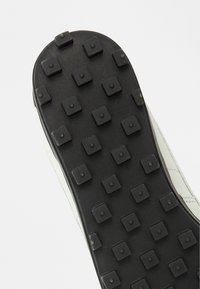 Σόλα παπουτσιού με μαύρη βάση από καουτσούκ και τετράγωνα εξογκώματα για πρόσφυση, συνδεδεμένη με ανοιχτόχρωμο, λείο υλικό στο επάνω μέρος.