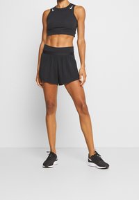 Svart sportig crop top med perforerade detaljer, kombinerad med löst sittande svarta shorts med bred midjeband och strukturerad tyg.