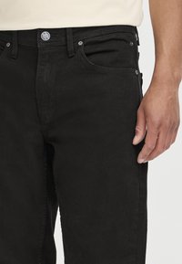Svart denimbukser med en glatt tekstur, fem-lommers design og metallbeslag med synlig frontknapp og glidelås.