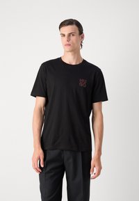Zwarte katoenen t-shirt met een rood "HUGO" logo op de linkerkant van de borst, ronde halslijn, korte mouwen en een ontspannen pasvorm.