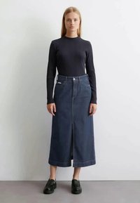 Σκούρο μπλε τζιν φούστα με μπροστινό άνοιγμα, ψηλή μέση και σχέδιο πέντε τσεπών. Συνδυασμένη με ένα εφαρμοστό μαύρο μπλουζάκι με μακριά μανίκια και μαύρα παπούτσια.