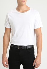 Hvid bomulds t-shirt med korte ærmer, parret med sorte jeans og et sort læderbælte med en sølvspænde. Glat tekstur, afslappet pasform.