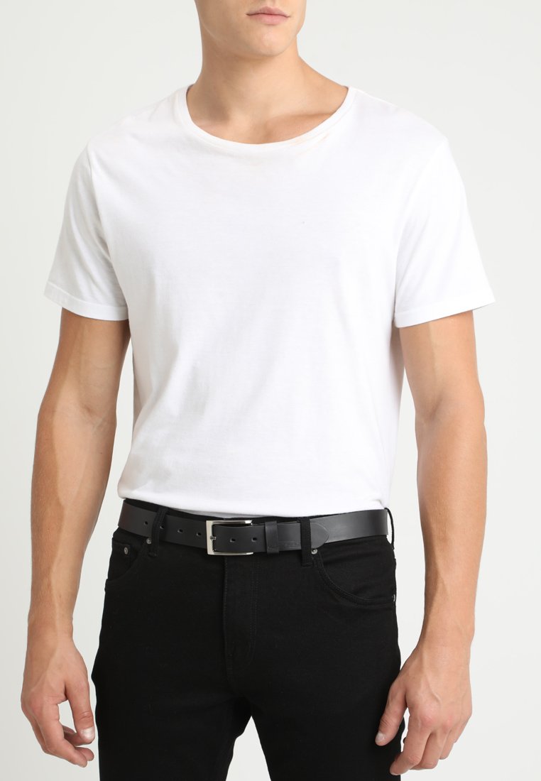Hvid bomulds t-shirt med korte ærmer, parret med sorte jeans og et sort læderbælte med en sølvspænde. Glat tekstur, afslappet pasform.