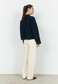 Pulover texturat bleumarin cu croială supradimensionată și umeri căzuți, asortat cu pantaloni largi crem și ghete maro de gleznă, privit din spate.