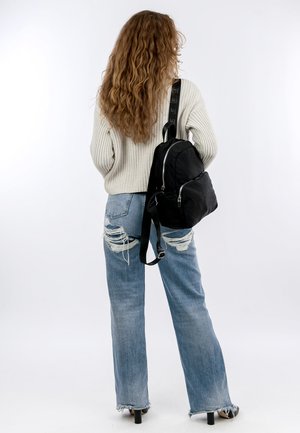 Schwarzer Stoffrucksack mit silbernen Reißverschlussdetails; kombiniert mit hellblauen, distressed Jeans und einem gestrickten cremefarbenen Pullover. Schlichtes Design.