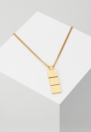 Złoty łańcuszek z prostokątnym wisiorkiem podzielonym na trzy gładkie, poziome segmenty, wyświetlany na białym geometrycznym bloku.