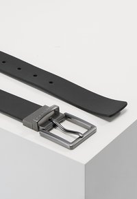 Cintura in pelle nera con finitura testurizzata, dotata di una fibbia in metallo opaco e diversi fori di regolazione lungo la cinghia.