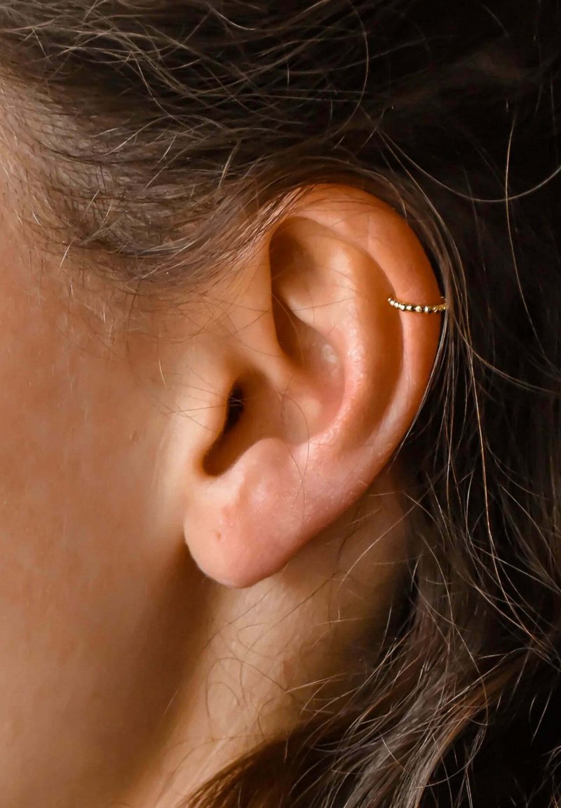 Boucle d'oreille en or avec un design texturé, portée sur la partie supérieure d'une oreille, mettant en valeur une peau lisse et de fins brins de cheveux.
