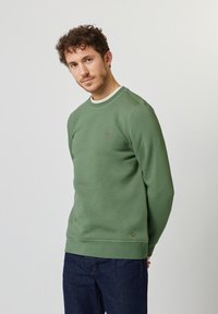 Grüner Pullover mit rundem Ausschnitt, gerippten Bündchen und Saum. Verfügt über ein kleines Baumlogo, das auf der Brust gestickt ist. Lässiges Design und dicke Textur.