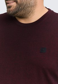 Bordeaux crewneck t-shirt van textuurstof, met een klein zwart logo patch op de borst. Casual ontwerp, zachte stof.