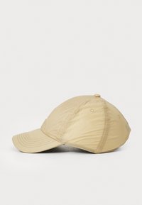 Cappellino da baseball beige realizzato in tessuto leggero, con visiera curva, dettagli cuciti e un bottone decorativo sulla parte superiore.