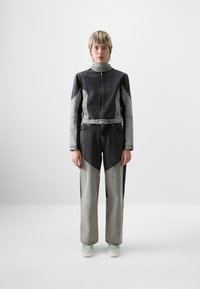 Mono de mezclilla en gris oscuro y gris claro, con un cierre frontal, paneles en contraste y un diseño ajustado. Acompañado de zapatos claros.