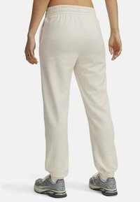 Lichtgrijze sweatpants met een zachte textuur en een elastische tailleband. Heeft zijzakken en taps toelopende manchetten. Gecombineerd met grijze sportschoenen.