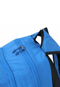 Sac à dos bleu en tissu texturé, avec double zippers dotés de tirants en caoutchouc et de bretelles noires. Le design comprend un motif en grille sur la surface.