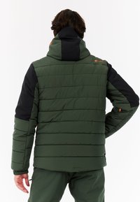 Giacca imbottita verde con cappuccio nero, caratterizzata da sezioni trapuntate, polsini regolabili e un dettaglio del logo arancione sulla spalla.