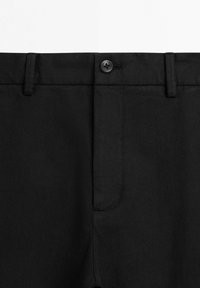 Primo piano della cintura di pantaloni neri con bottone, passanti per cintura e chiusura a zip.