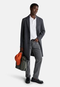Abrigo de lana gris sobre una camiseta polo blanca, pantalones vaqueros grises, zapatos negros, gorra naranja y bolsa verde. Presenta texturas y contrastes de color destacados.
