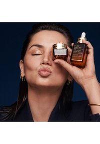 Deux produits Estée Lauder : un pot transparent avec un couvercle doré étiqueté "Advanced Night Repair Eye" et une bouteille en verre brun avec un compte-gouttes étiquetée "Advanced Night Repair."