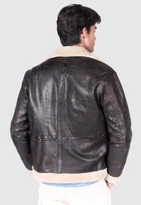 Brun läderjacka med texturerad yta, fårskinnskrage och krämfärgad foder. Har dragkedjestängning och två sidofickor.