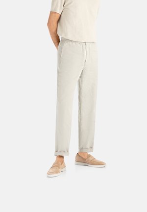 Lyse beige bukser lavet af blødt stof, med en afslappet pasform og synlige sømme, parret med lysebrune slip-on sko.