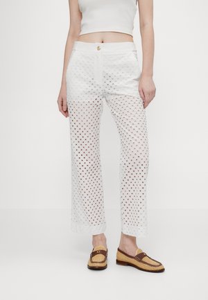 Pantaloni bianchi a fantasia con ritagli a forma di diamante, vita alta e chiusura con bottone. Abbinati a scarpe slip-on in pelle intrecciata marroni.
