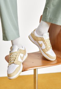 Nike-sneakers med en beige och vit färgskala, läder- och meshmaterial, texturerad ovandel och framträdande logotyp.