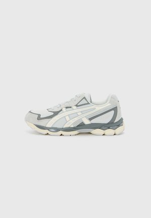 Scarpa sportiva grigio chiaro con un mix di materiali in rete e suede, dotata di strisce bianche, suola imbottita e design della punta arrotondato.