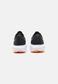Chaussures de sport noires avec une tige texturée, une semelle intermédiaire blanche et des accents orange sur la semelle extérieure. Comprend des rayures vertes sur les côtés et des tirettes.