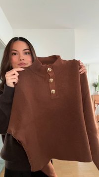 Pull en maille marron avec col haut et trois accents de boutons dorés. Caractérisé par une texture douce et une coupe légèrement oversized.