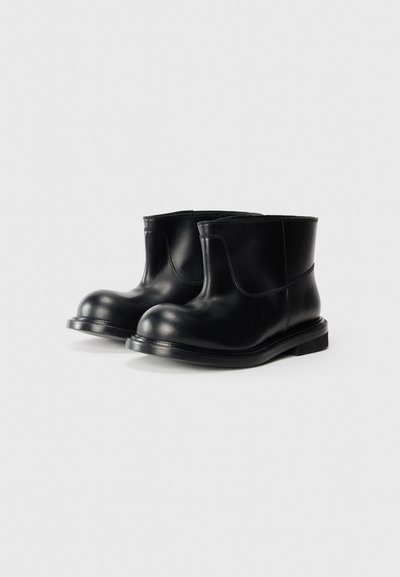 Botas de cuero negras hasta el tobillo con puntera redondeada, textura suave, tacón bajo y diseño simple. Sin herrajes ni adornos visibles.